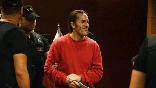 Juan Aliste in a courtroom, surrounded by police officers